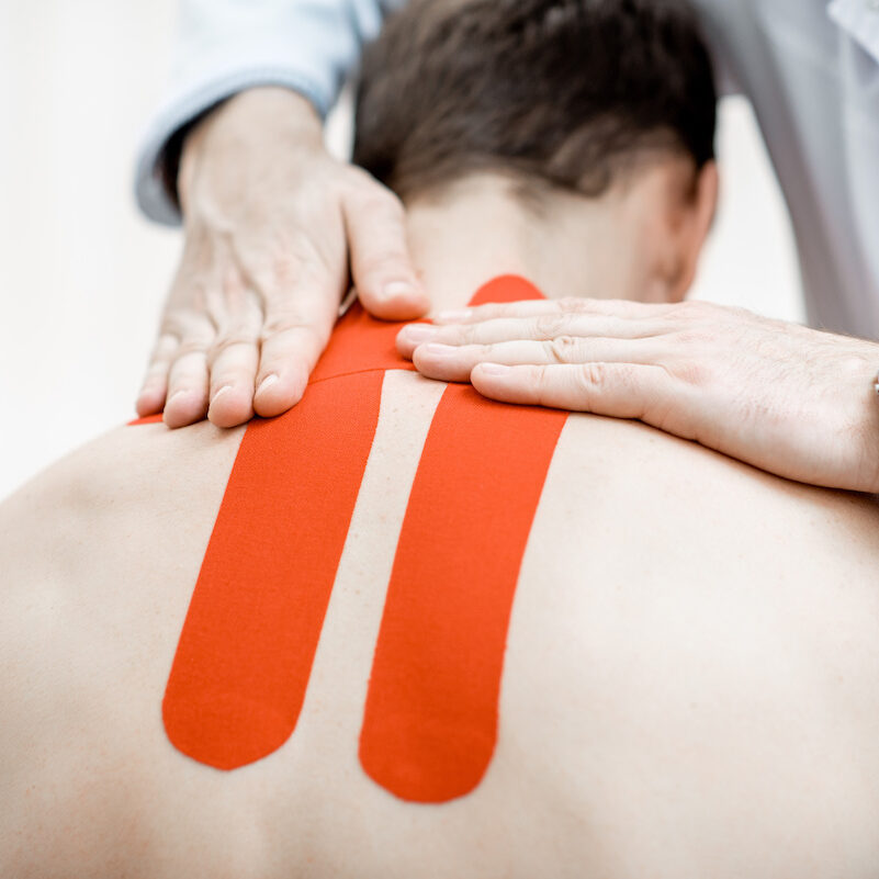 Senior therapist applying kinesio tape on a man's neck during the medical treatment in the office